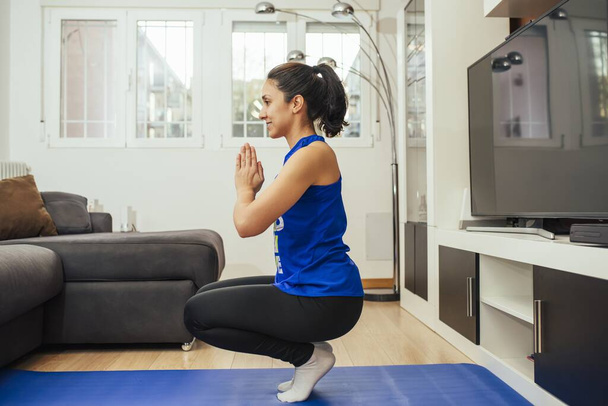 A female training at home and doing yoga asana on a blue matt - Фото, изображение