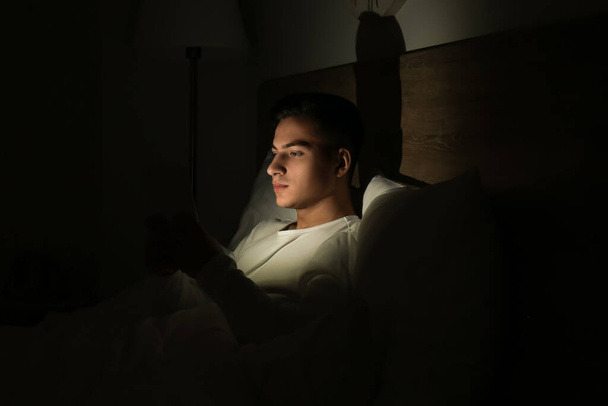 Νεαρός άνδρας που πάσχει από στέρηση ύπνου με tablet υπολογιστή στο υπνοδωμάτιο τη νύχτα - Φωτογραφία, εικόνα
