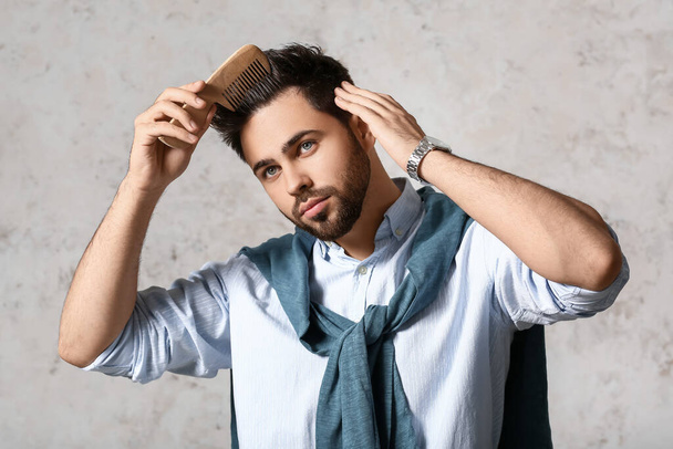 Handsome man combing hair on light background - Foto, immagini