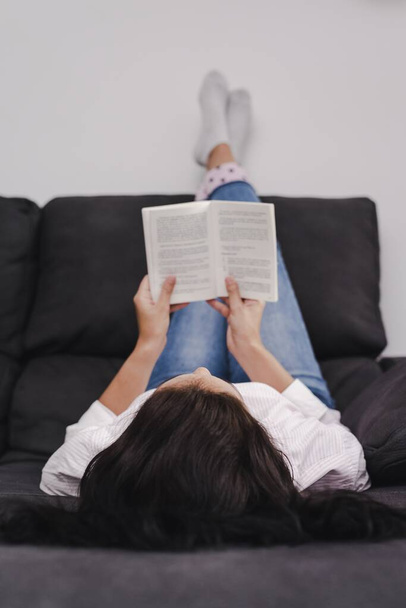 A young female lying with feet lying on the wall reading a book - Фото, зображення