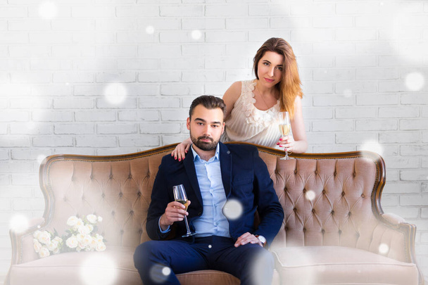 coppia felice con bicchieri di champagne seduti sul divano vintage a casa e fiocchi di neve che cadono - Foto, immagini