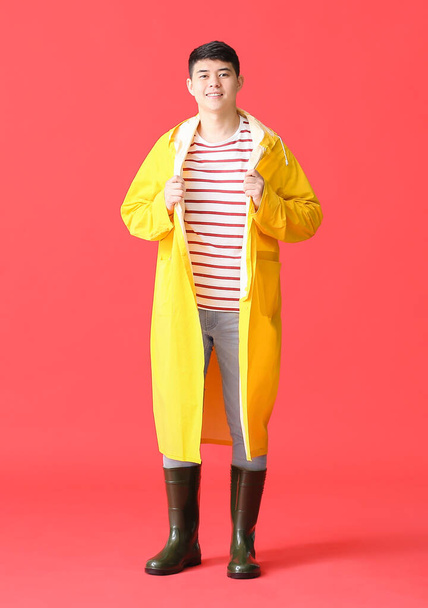 Young Asian man in raincoat on color background - Foto, immagini