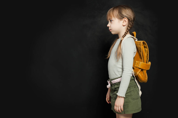 Trauriges Schulmädchen mit Rucksack auf schwarzem Hintergrund. Schulproblem-Konzept - Foto, Bild