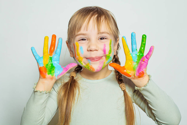 Boldog mosolygós gyermek lány művészeti iskolában tanuló mutatja neki színes festett kezét fehér. Lányrajz - Fotó, kép