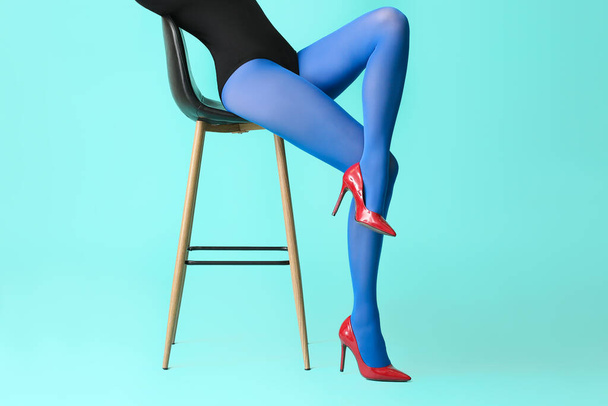 Beautiful young woman in tights sitting on chair against color background - Φωτογραφία, εικόνα