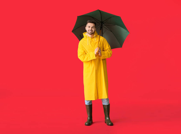 Young man in raincoat and with umbrella on color background - Fotografie, Obrázek