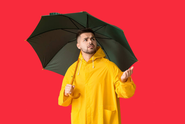 Young man in raincoat and with umbrella on color background - Foto, Imagen