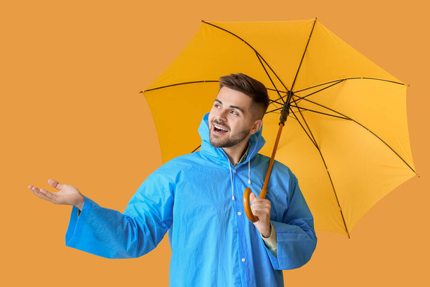 Young man in raincoat and with umbrella on color background - Photo, image