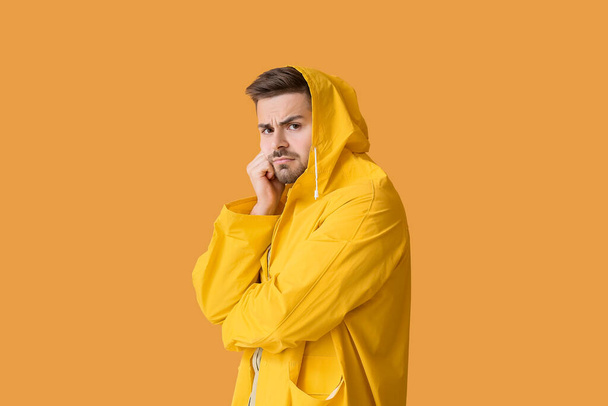 Displeased young man in raincoat on color background - Фото, изображение