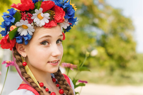 Sulje muotokuva tyttö, jolla on kaksi punokset Ukrainan perinteisiä kukkia seppele nauhoilla, punainen korvakorut ja helmiä. Päänlaukaus epäselvä ulkona tausta, kopioi tilaa.  - Valokuva, kuva