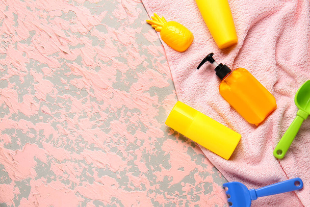 Zonnebrandcrème met strand zand speelgoed en handdoek op kleur achtergrond - Foto, afbeelding