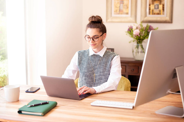 Shot of smiling businesswoman sitting behind her laptop while working from home. Home office. - Foto, Imagem