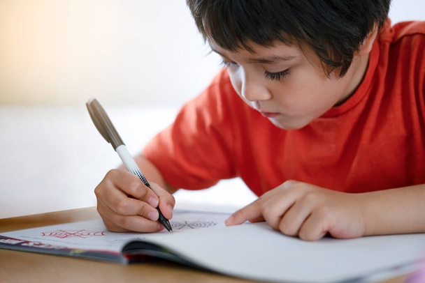 Enfoque selectivo del niño de la escuela sentado en la mesa haciendo la tarea, niño feliz sosteniendo la pluma negra, niño pequeño está escribiendo en el papel blanco, escuela primaria, concepto de educación en el hogar
 - Foto, imagen