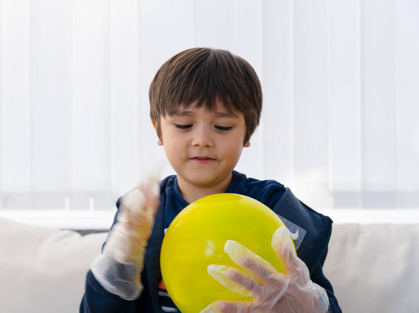 Выборочный фокус ребенка носить одноразовые защитные пластиковые перчатки и держа желтый воздушный шар, ребенок готовит научный проект о статических заряженных, ребенок с любопытством смотрит на научные эксперименты, Главная школа концепции
 - Фото, изображение