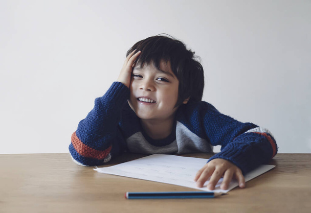 Portrait von Smart Kind Spaß bei den Hausaufgaben, Kind Junge Blick in die Kamera mit lächelndem Gesicht glücklich nach der Schule Hausaufgaben abgeschlossen. Positives Kind, Homeschooling-Konzept - Foto, Bild