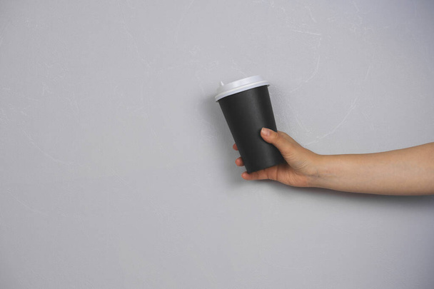 female hand holding coffee to go blank cup against concrete gray wall copy space - 写真・画像