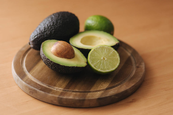 Avocado and lime halves on wooden board. Vegetarian food concept - Photo, Image