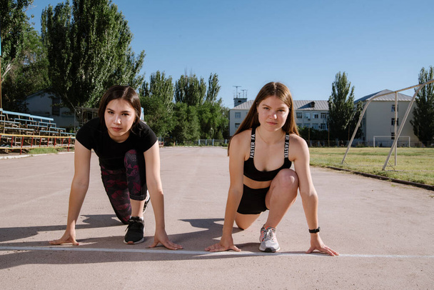 Two athletes at the starting position in the stadium. Athletic girls run in the stadium.Girls are doing exercises, stretching. Sport and healthy lifestyle. - Foto, afbeelding