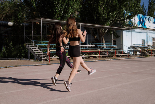 athletic girls are running, athletic girls are running at stadium.Young women running during sunny morning on stadium track.Girls are doing exercises, stretching. Sport and healthy lifestyle. - Fotografie, Obrázek
