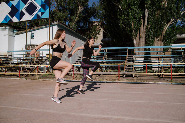 athletic girls are running, athletic girls are running at stadium.Young women running during sunny morning on stadium track.Girls are doing exercises, stretching. Sport and healthy lifestyle. - Foto, Imagem