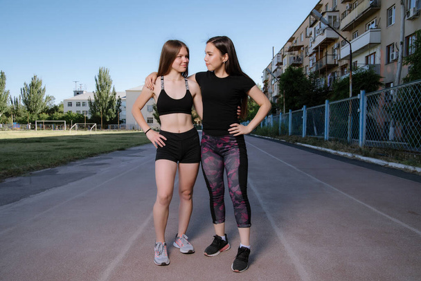 Two girls in sportswear posing at the stadium.Portrait of two sports girlfriends at the sports stadium.Sport and healthy lifestyle. - Φωτογραφία, εικόνα