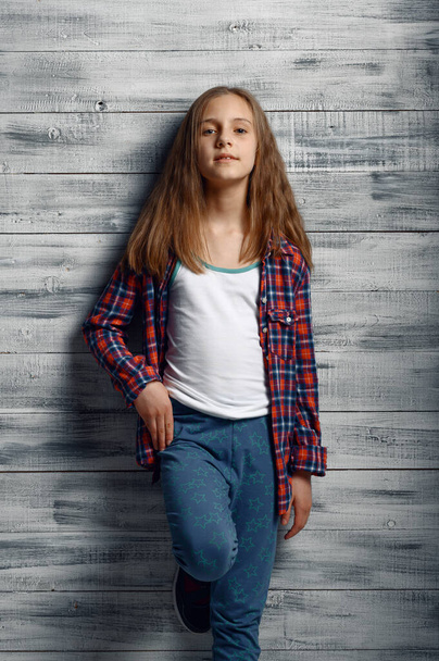 Adorable little girl standing at the wall in studio. Kid isolated on wooden background, child emotion, schoolgirl photo session - Φωτογραφία, εικόνα