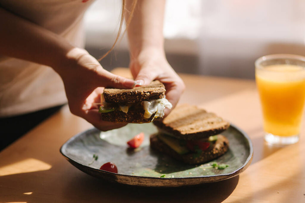 La donna tiene in mano un sandwich morso. Pane tostato di segale con avocado. Succo d'arancia fresco Cibo vegano
 - Foto, immagini