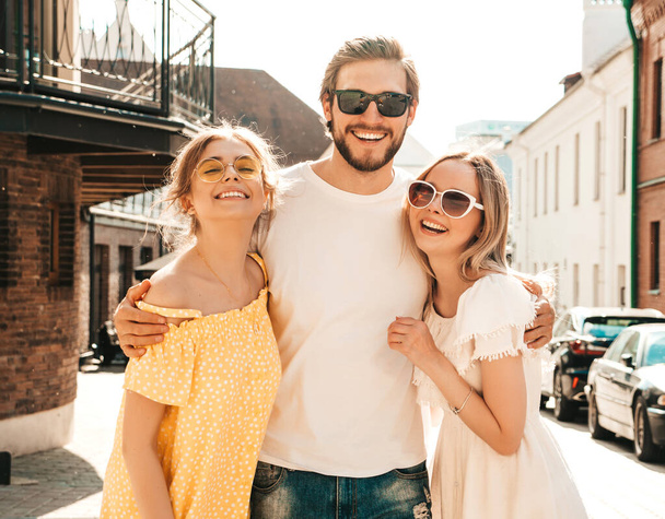 Group of young three stylish friends posing in the street. Fashion man and two cute girls dressed in casual summer clothes. Smiling models having fun in sunglasses.Cheerful women and guy going crazy - Zdjęcie, obraz