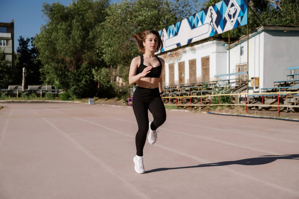 athletic girl is running,athletic girl is running at stadium.Young woman running during sunny morning on stadium track.Girl is doing exercises, stretching. Sport and healthy lifestyle. - Foto, Bild