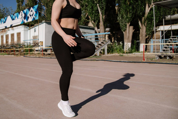 athletic girl is running,athletic girl is running at stadium.Young woman running during sunny morning on stadium track.Girl is doing exercises, stretching. Sport and healthy lifestyle. - Valokuva, kuva