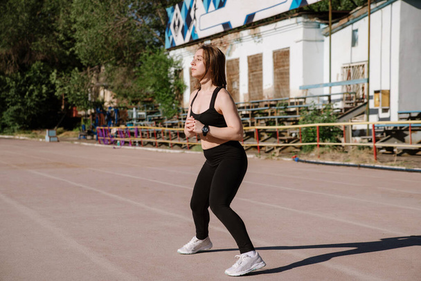athletic girl is running,athletic girl is running at stadium.Young woman running during sunny morning on stadium track.Girl is doing exercises, stretching. Sport and healthy lifestyle. - 写真・画像