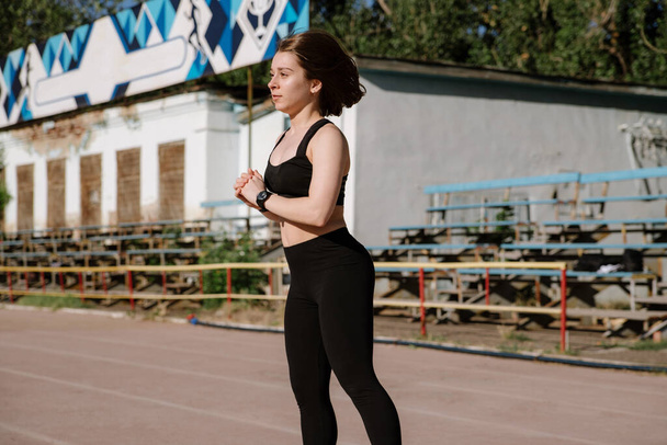 athletic girl is running,athletic girl is running at stadium.Young woman running during sunny morning on stadium track.Girl is doing exercises, stretching. Sport and healthy lifestyle. - Foto, afbeelding
