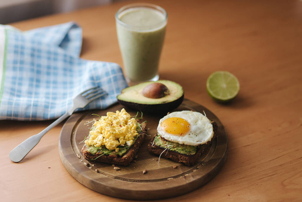 Verschiedene gekochte Eier auf Avocado-Sandwich mit Vollkornbrot auf Holzbrett. Smoothie mit Spinat - Foto, Bild