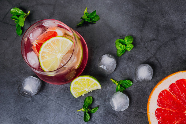Sitrushedelmien kylmä cocktail läpinäkyvissä laseissa tummalla taustalla. Noin viipaleet appelsiinia, sitruunaa, greippiä, jäätä ja minttua. Top view, tasainen lay, minimalismi Käsite kesän sitrushedelmien virvoitusjuoma, cocktail - Valokuva, kuva