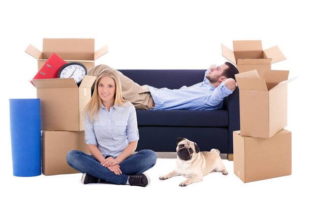 Moving Day concept - vermoeid jong paar met bruine kartonnen dozen met spullen en hond geïsoleerd op witte achtergrond - Foto, afbeelding