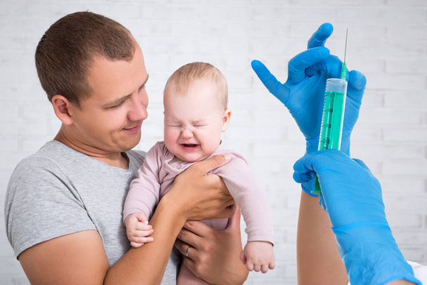 Gesundheitsversorgung und Impfkonzept - junger Vater hält weinendes Baby und Ärztin mit Spritze in den Händen - Foto, Bild