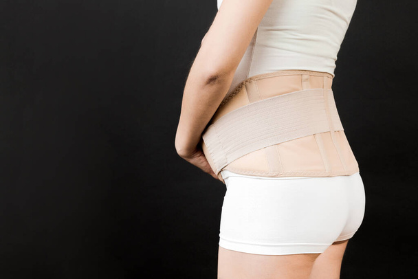 Side view of pregnant woman wearing pregnancy belt at black background with copy space. Close up of orthopedic abdominal support belt concept. - Photo, Image