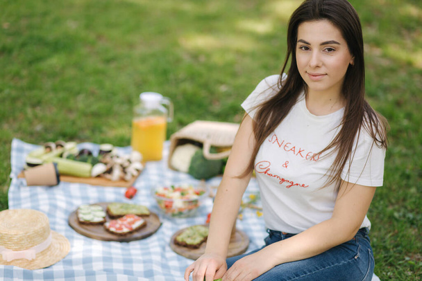 Веганский пикник на открытом воздухе. Женщина берет веганский сэндвич со свежими овощами. Пространство для текста. Веганский пикник
 - Фото, изображение