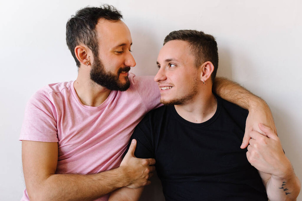 Archivbild zweier kaukasischer homosexueller Männer, die sich in ihrer Wohnung anschauen. Einer umarmt den anderen von hinten. - Foto, Bild