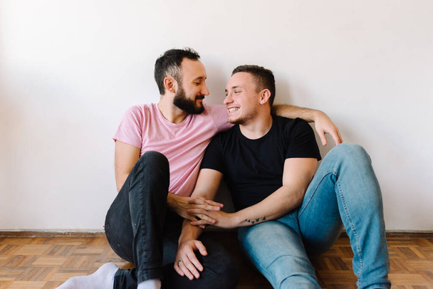 Stockfoto van twee blanke homoseksuele mannen gelukkig in hun appartement. Een van hen omhelst de andere van achteren.. - Foto, afbeelding