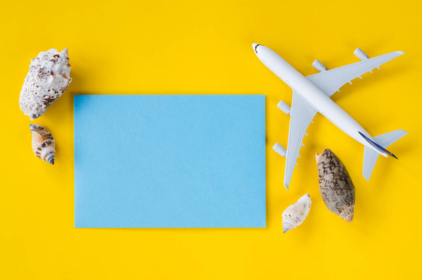 Papier bleu vide sur fond jaune avec coquillages et avion décoratif. Concept de voyage d'été. Vue de dessus ou à plat. Espace de copie. - Photo, image