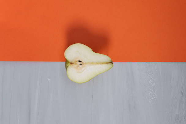 Über reife halbgrüne köstliche Birne vor orangefarbenem und grauem Hintergrund. Design-Vorlage, organisches Konzept - Foto, Bild