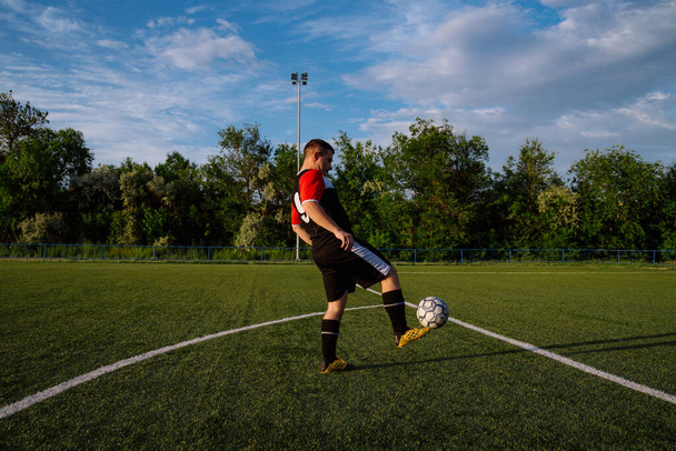 Молодий футболіст жонглює м'яч на футбольному полі. Спортсмен жонглює футбол ногами на стадіоні.
 - Фото, зображення