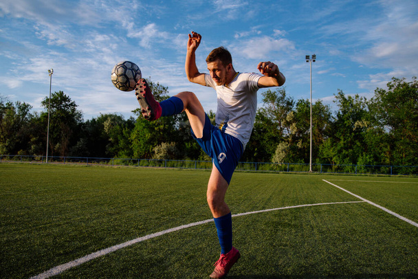 Young male soccer player juggles a ball on a soccer field.Athlete juggling the football with his feet in stadium.Football sports concept - Photo, Image