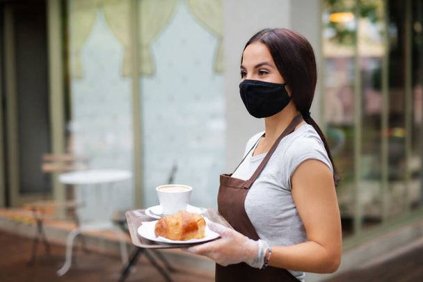 Young woman with face mask working in cafe, serving customers. - Photo, Image