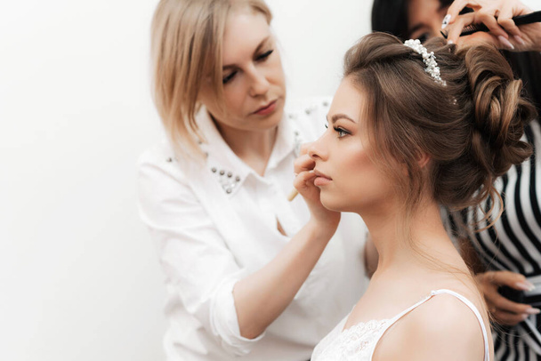 morning preparations for the brides wedding in a beauty salon. A makeup artist does make-up and a hairdresser does her hair - Valokuva, kuva
