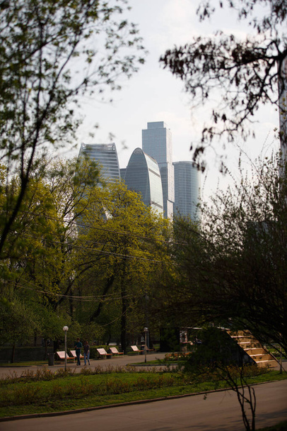 MOSCOW / RUSSIA - 20/04/2019 vertical distant cityscape day view of the tops of the Moscow City skyscrapers hidden behind tall trees, branches, green leaves. Shot from the Krasnaya Presnya urban park - Fotó, kép