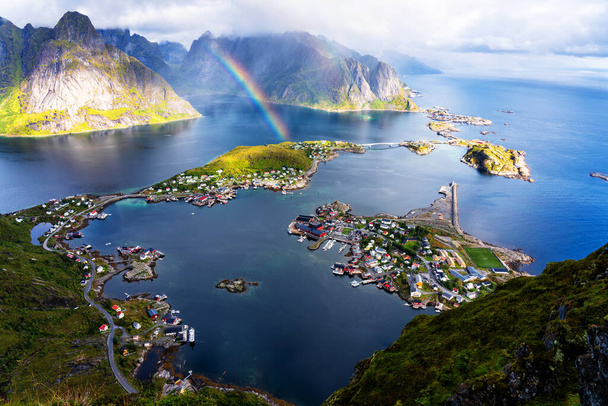 Vista panorâmica aérea ensolarada sobre montanhas deslumbrantes e aldeia de Reine em ilhas Lofoten, Noruega a partir de Reinebringen cume. Vista panorâmica com um arco-íris e picos acidentados
. - Foto, Imagem