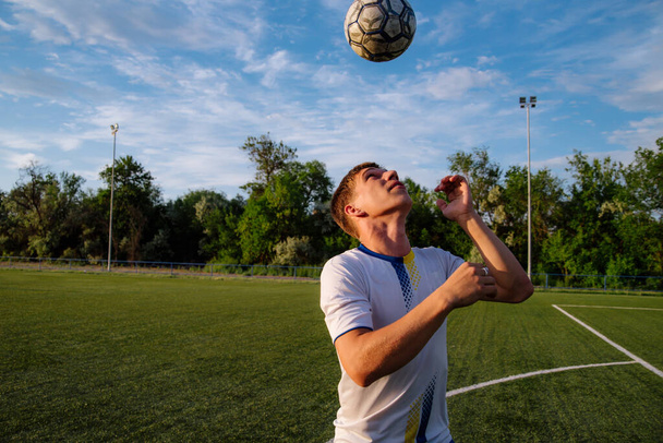 Young male soccer player juggles a ball on a soccer field.sport, football and people - soccer player playing and juggling ball using header technique on field.Football sports concept - Zdjęcie, obraz