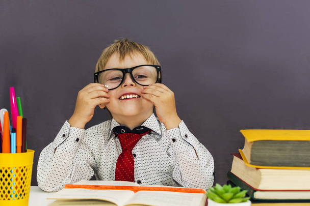 chico divertido inteligente con gafas en una mesa con libros sobre un fondo gris
 - Foto, imagen